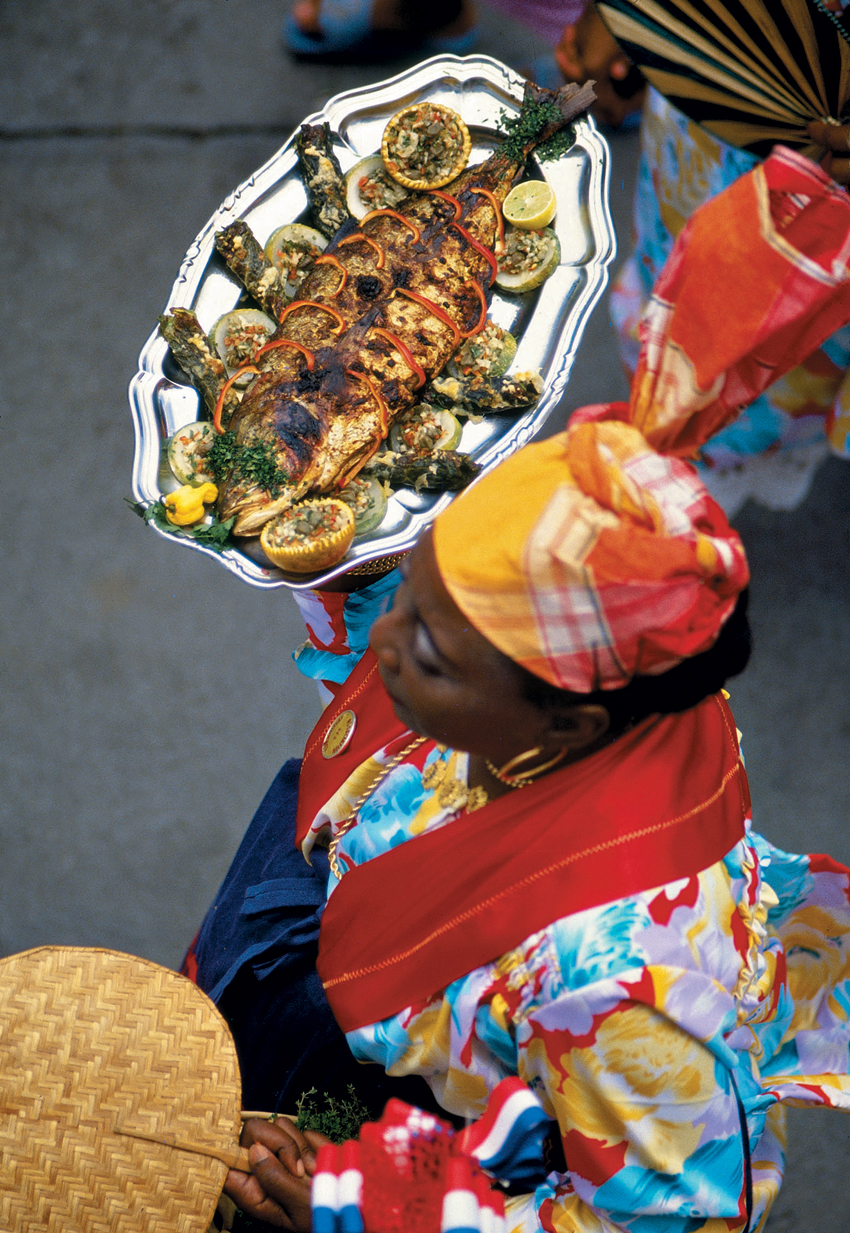Femme portant un plateau de poissons grillés lors de la Fête des cuisinières