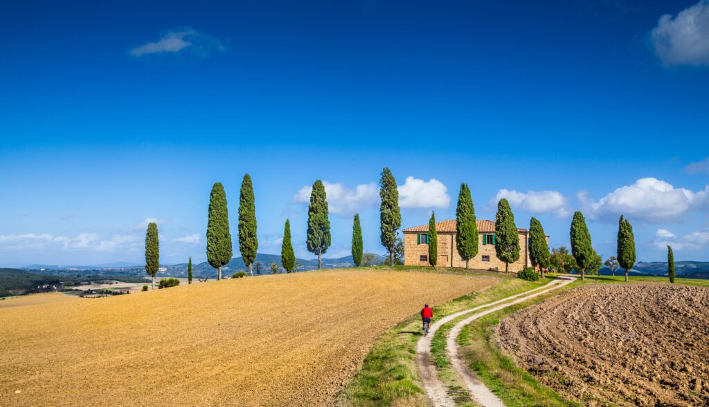 Scenic Tuscany landscape with farmhouse and cyclist on a sunny day, Italy