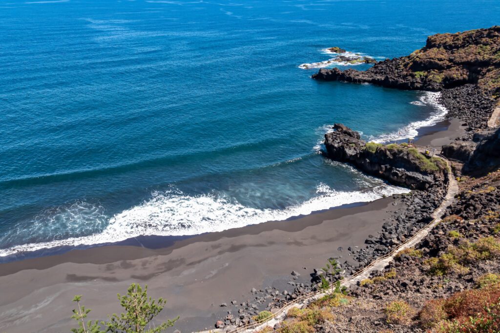 Panoramic aerial view on the dark fine lava sand beach Playa El Bollulo near near Puerto de la Cruz, Northern Tenerife, Canary Islands, Spain, Europe. Beautiful coastline with no people. Hiking trail