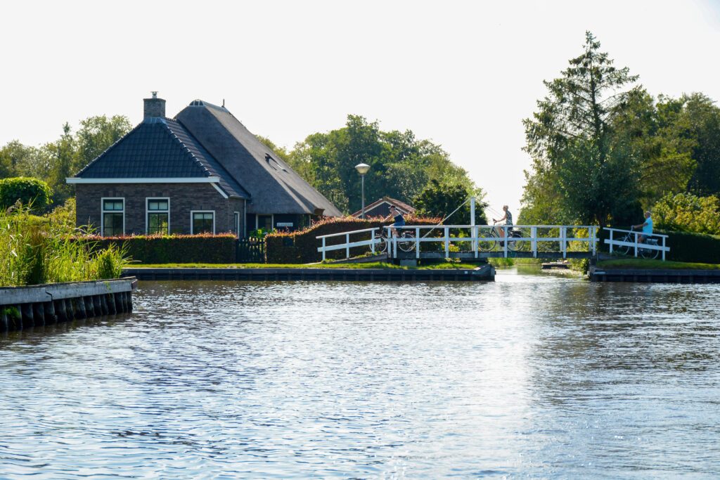 Beautiful scenery during summer with a small bridge and cycling tourists and with a typical dutch house next to the canal in Ossenzijl, National Park Weerribben-Wieden, Overijssel, The Netherlands.