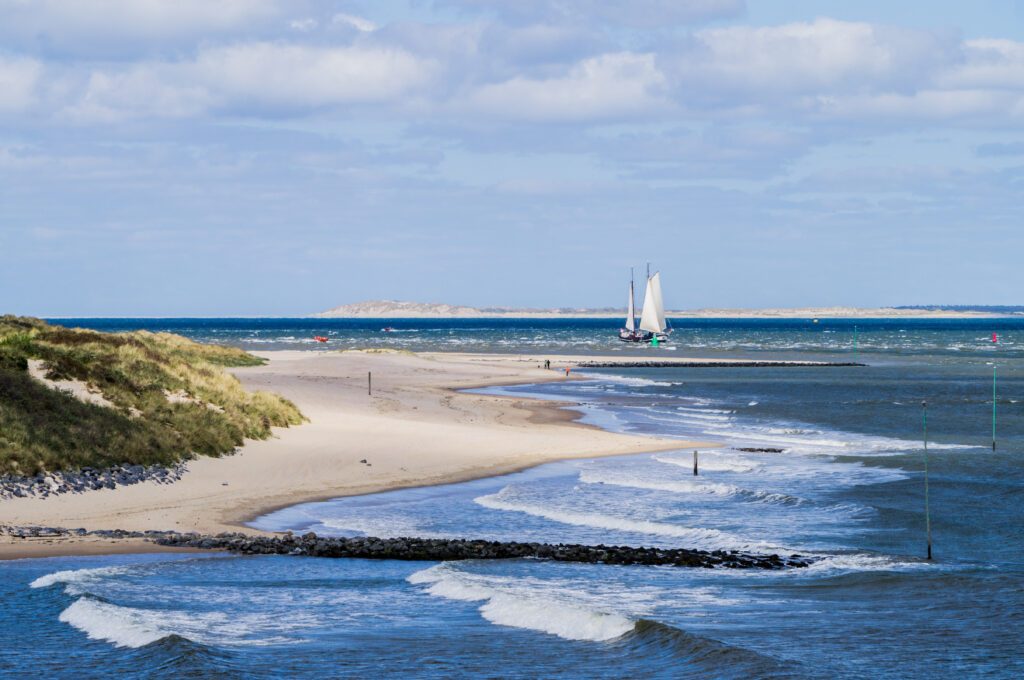 North sea seascape of seaside on Vlieland island with ground swell blue sea and big sailing vessel approaching the coast