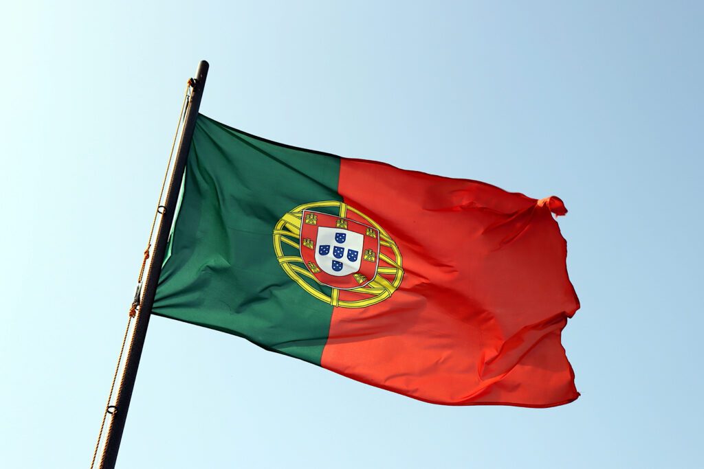 Red and green portuguese flag waving in the wind, against blue sky