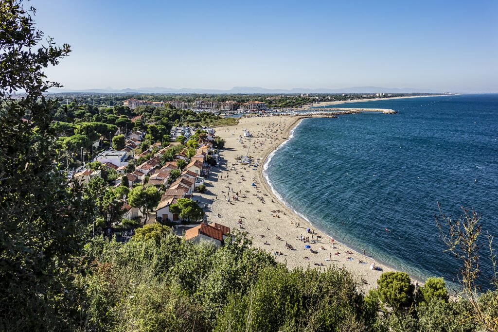 Sandy Mediterranean beach Le Racou in Argeles sur Mer with its old fishermens houses and the harbor in background, Roussillon, Pyrenees Orientales, France.