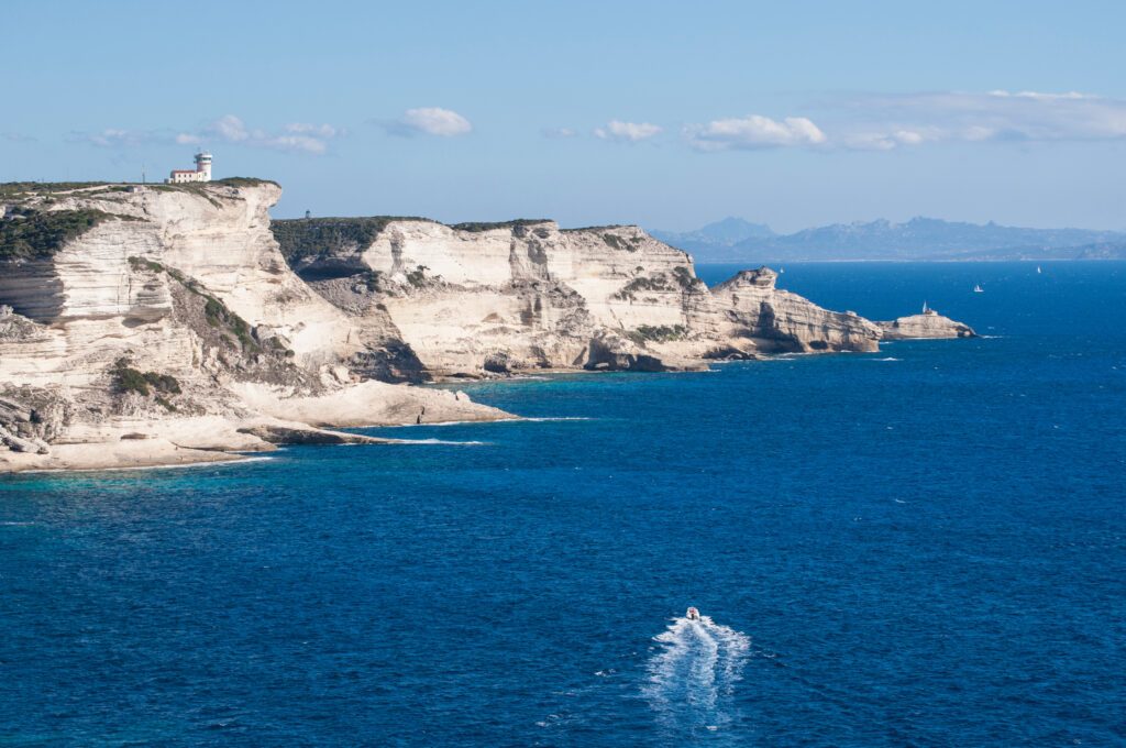 Corsica, 05/09/2017: le bianche scogliere di Bonifacio nella riserva naturale del Parco internazionale delle Bocche di Bonifacio, con vista del faro di Capo Pertusato