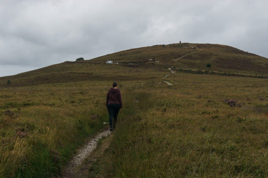 Woman hiking to the hill Mont Saint Michel de Brasparts with chapel on top on a cloudy autumn day, Parc naturel regional d'Armorique, Brittany, France