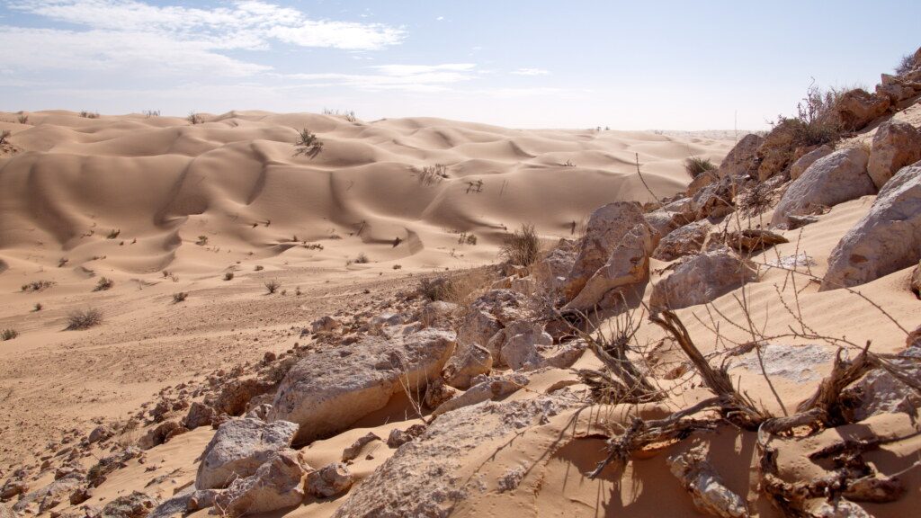 Rocky slope surrounded by sand dunes in the Sahara Desert, outside of Douz, Tunisia
