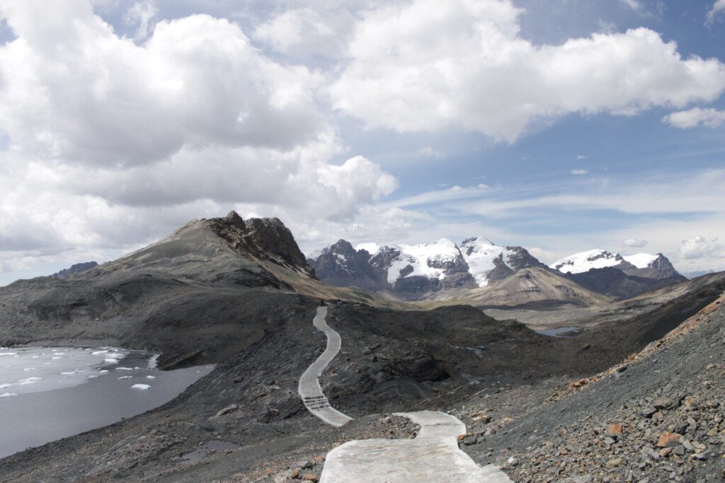 Glacier in huaraz peru, path to the snowy and icy mountains on the horizon, with a lake on the side from the way