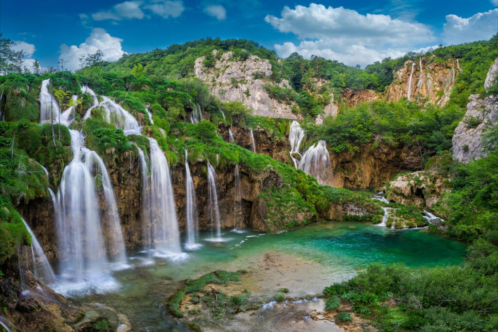 Plitvice, Croatia - Beautiful waterfalls of Plitvice Lakes (Plitvička jezera) in Plitvice National Park on a bright summer day with blue sky and clouds and green foliage and turquise water