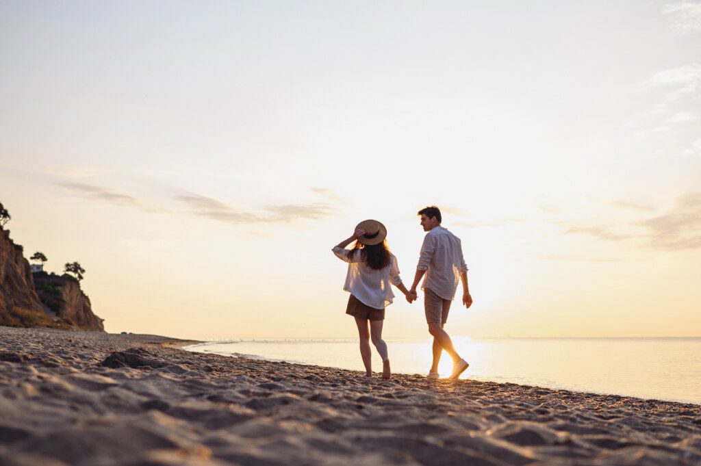 Full body back rear view young couple two friends family man woman in white shirt clothes hold hands walk stroll together at sunrise over sea beach ocean outdoor exotic seaside in summer day evening.