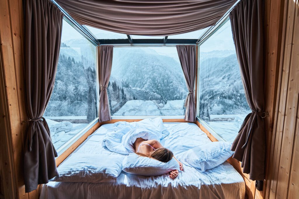 Tranquil serene calm woman sleeping on a soft white cozy comfortable warm bed in room with snowy winter mountains view