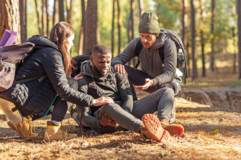 Friends helping african injured guy while hiking by forest