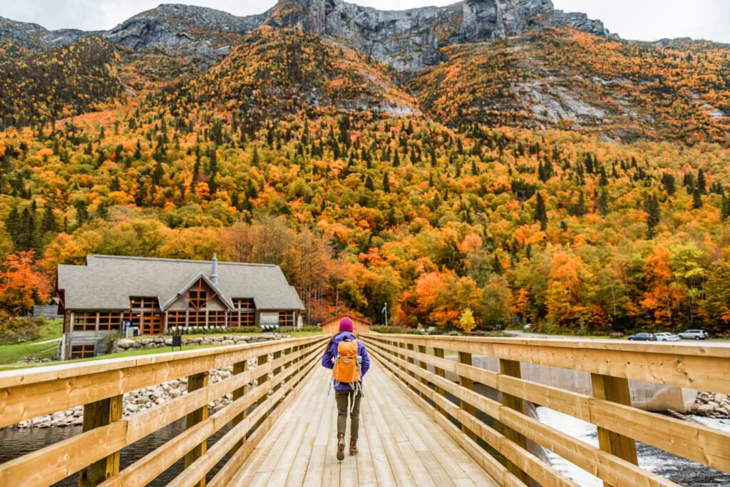 Autumn nature hiker girl walking in national park in Quebec with backpack. Woman tourist going camping in forest. Canada travel hiking tourism at Hautes-Gorges-de-la-Riviere-Malbaie National Park.