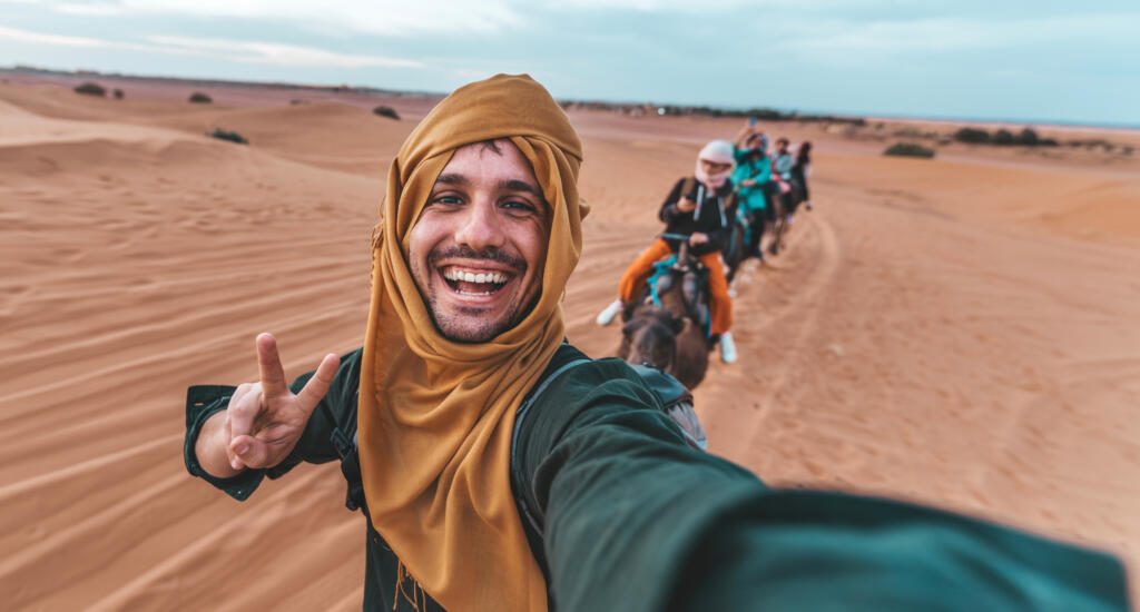 Happy tourist having fun enjoying group camel ride tour in the desert - Travel, life style, vacation activities and adventure concept