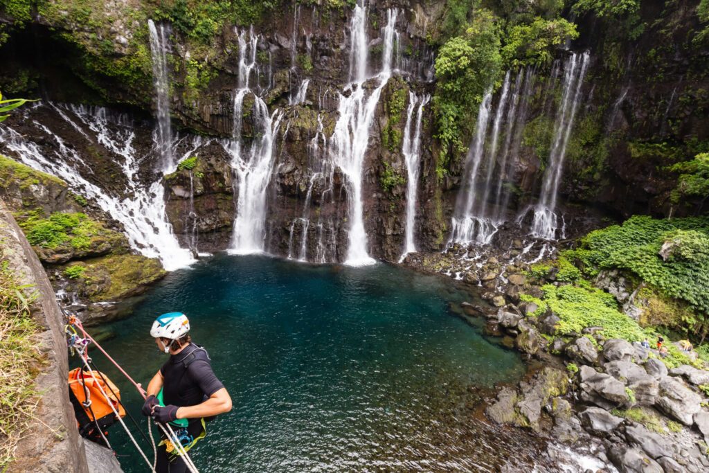 Homme se préparant à une descente en rappel sur une paroi pour du canyoning, devant de magnifiques cascades. Rivière Langevin, Réunion