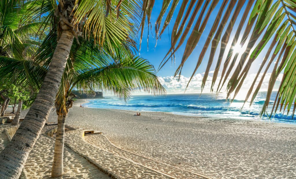 Wide view of the sunrise in Boucan Canot beach in the summertime, with blue sea water and yellow sand in Reunion