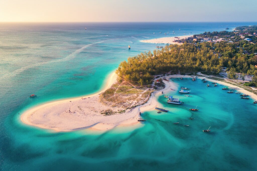 Aerial view of the fishing boats on tropical sea coast with sandy beach at sunset. Summer holiday on Indian Ocean, Zanzibar, Africa. Landscape with boat, green trees, transparent blue water. Top view