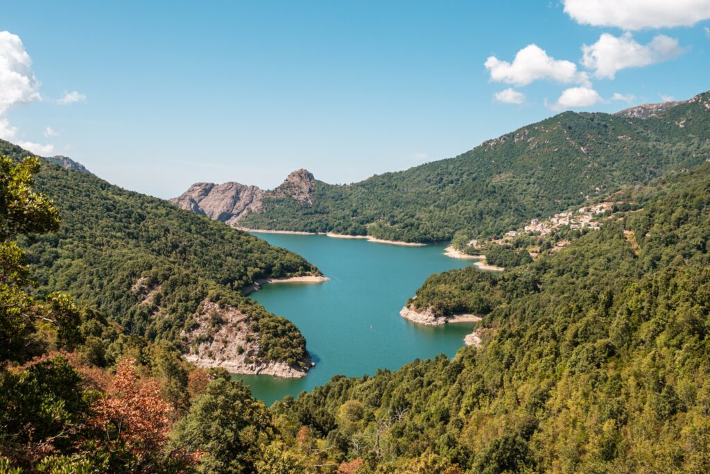 The dam wall at Lac de Tolla in Corsica surrounded by rocky cliffs and pine forest with mountains in the distance