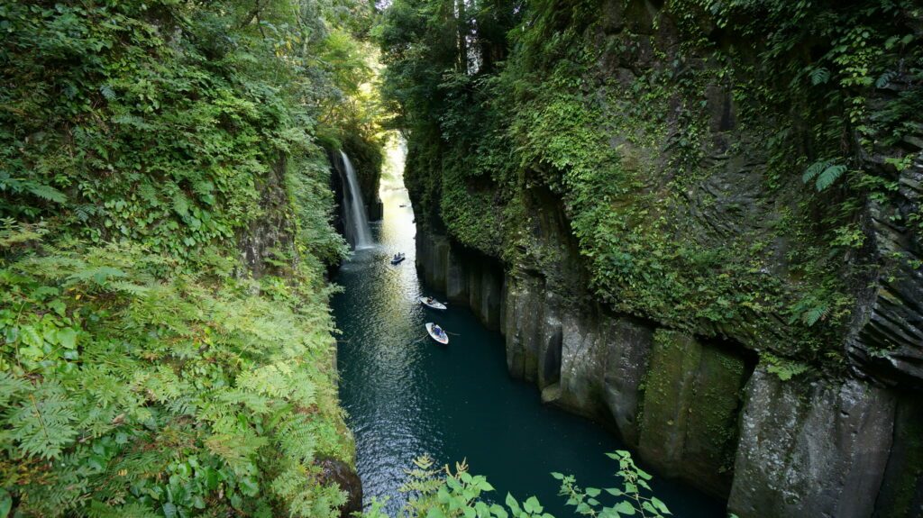 Boats are floating in Takachiho Gorge on Gokase River around Minainotaki waterfall, Japan. Romantic activity for tourists and couples.