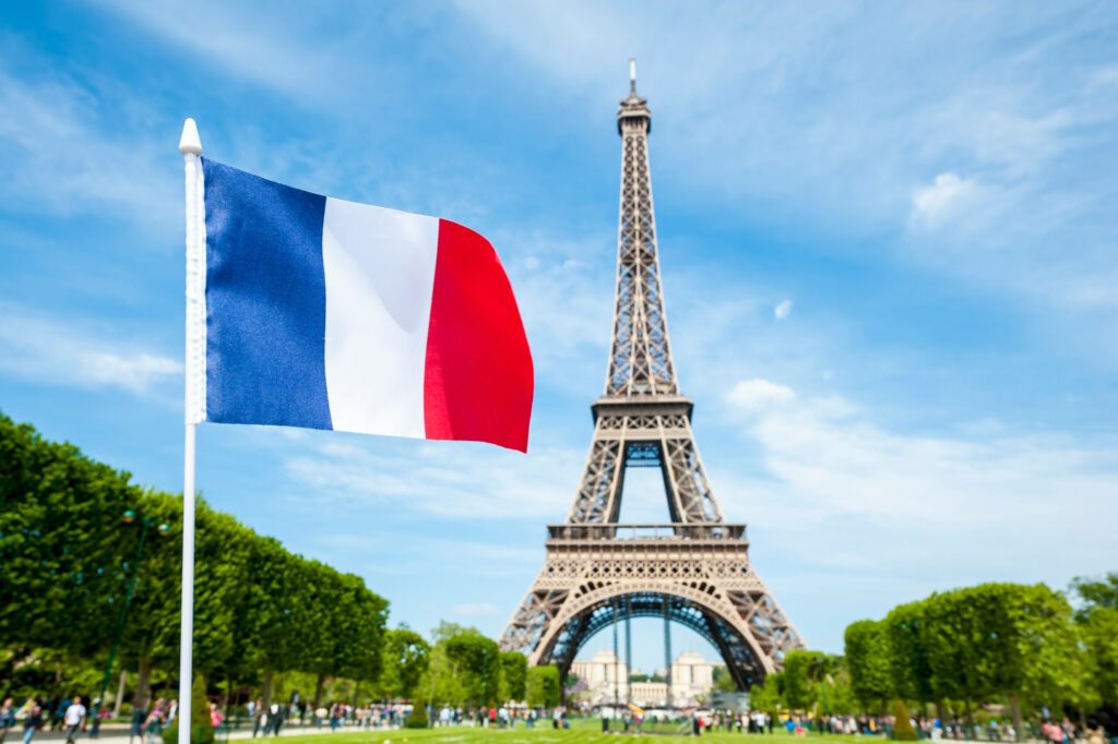 French flag flying in bright blue sky above the Eiffel Tower in Paris, France