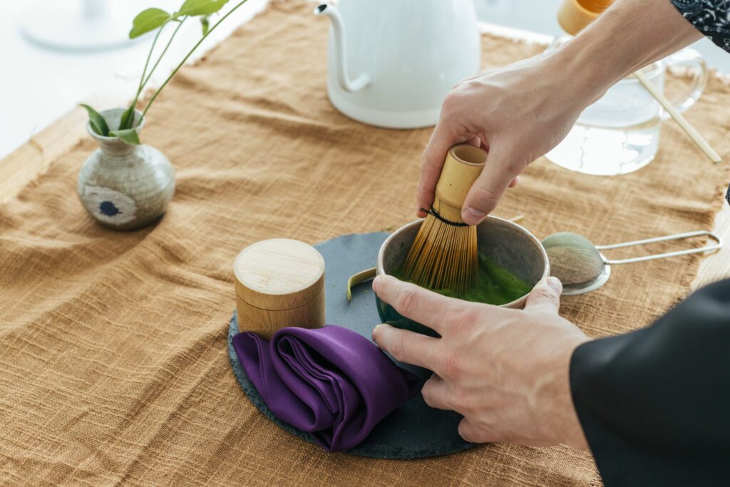 Traditional Japanese green tea match close-up. Matcha tea ceremony, a bamboo Chassen whisk for whipping and tea in a bowl on the brown background.