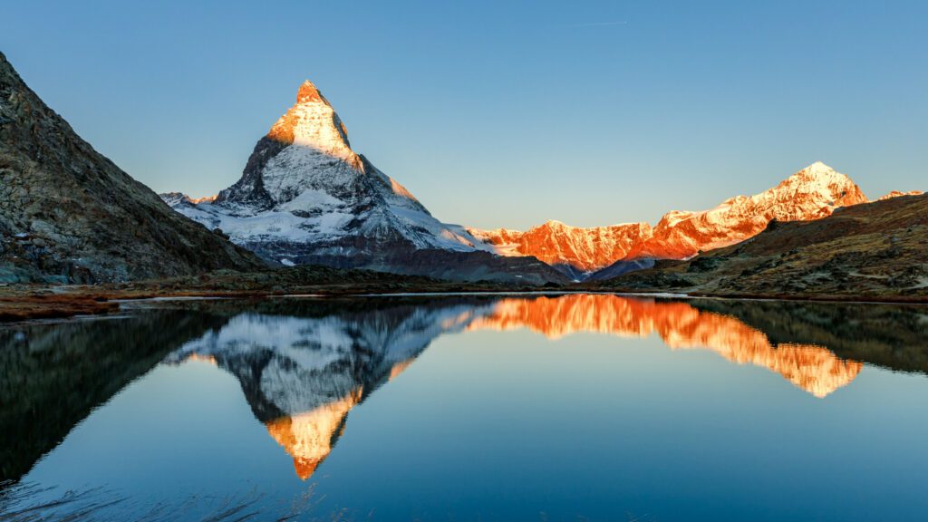 Classical Swiss view of snow-capped epic Mattergorn mountain peak reflected in Riffelsee lake. Iconic landmark in Switzerland located near Zermatt resort. Picturesque landscape of alpenglow in Alps.
