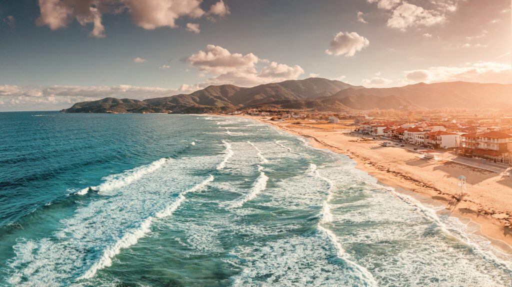 Dramatic panoramic aerial view of iconic Sarti resort town and famous long and empty sandy beach at sunset time with high waves. Vacation on Halkidiki, Greece