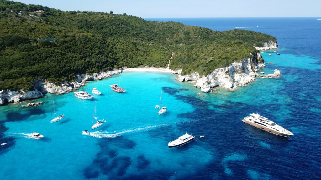 Aerial drone photo of tropical paradise turquoise beach of Voutoumi with sail boats docked in island of Anti paxos, Ionian, Greece