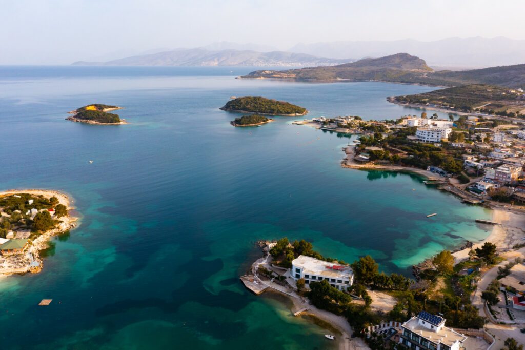 Scenic aerial view of Albanian coast of Ionian Sea overlooking green Ksamil Islands in turquoise water and cityscape on shore in spring