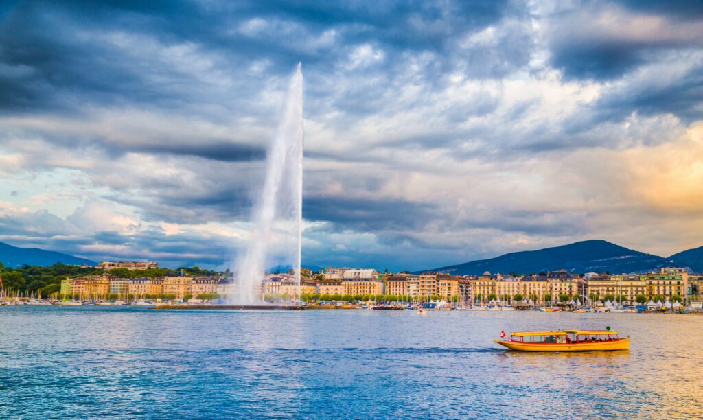 Geneva skyline with famous Jet d'Eau fountain and boat at sunset, Switzerland