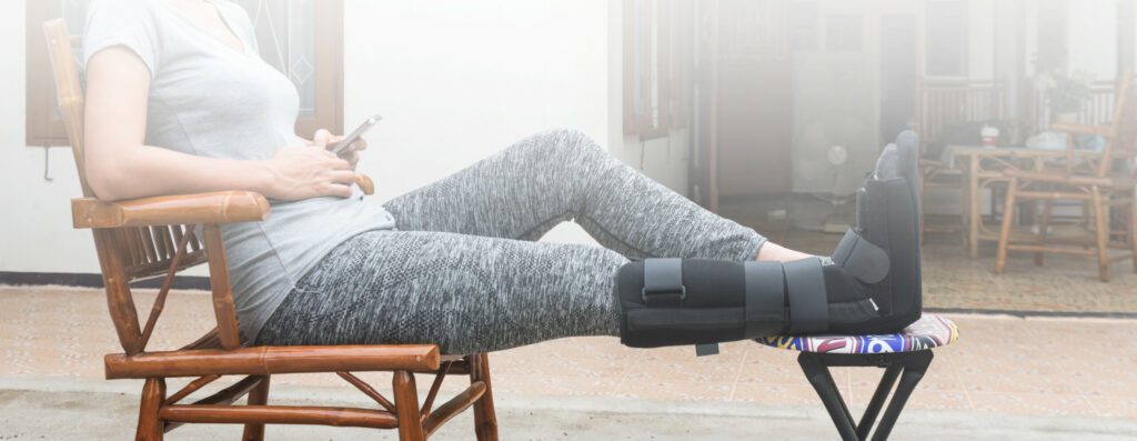 woman with black cast on leg sitting on wood chair, body injury concept