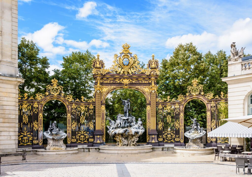 The fountain of Neptune in the Rococo style and the gilded wrought iron portico in the north-west corner of the Stanislas square in Nancy, France.