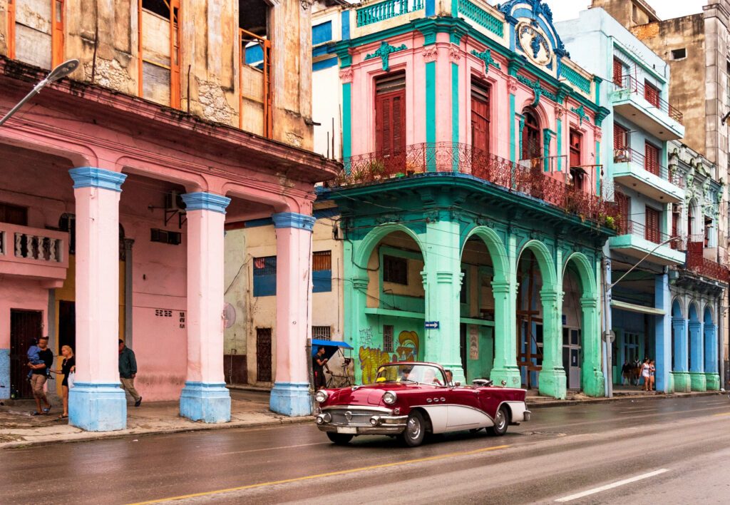 convertible classic car in front of colorful houses in havana cuba