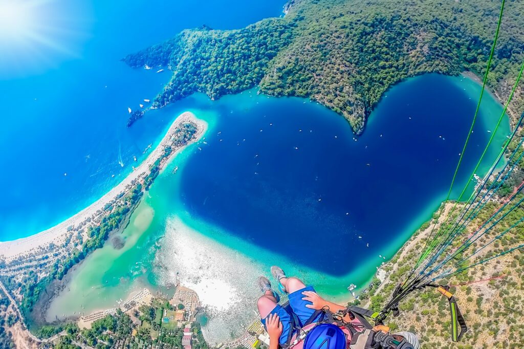 Extreme sport. Landscape . Paragliding in the sky. Paraglider tandem flying over the sea with blue water and mountains in bright sunny day. Aerial view of paraglider and Blue Lagoon in Oludeniz, Turke