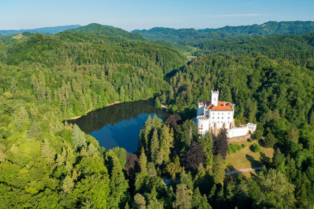 Aerial view of Trakoscan castle surrounded by the lake and forested hills, rural Croatia