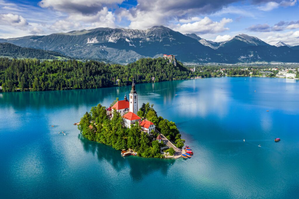 Bled, Slovenia - Aerial view of Lake Bled (Blejsko Jezero) with the Pilgrimage Church of the Assumption of Maria, pletna boats, Bled Castle and Julian Alps on a sunny summer day